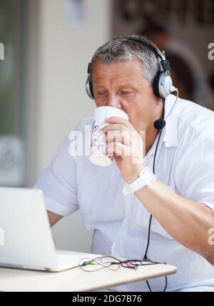 Man Drinking Coffee and Using Laptop at Cafe Stock Photo