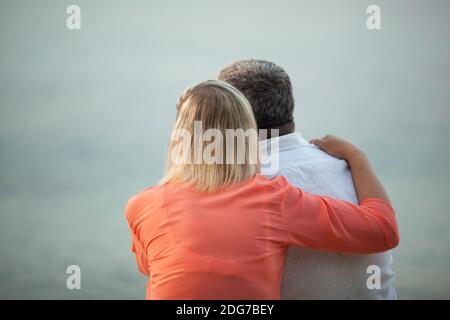 Couple with Arms Around Each Other Admiring Sunset Stock Photo