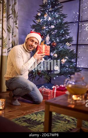 Handsome bearded male in casual clothes feeling surprised with gift in arms in room indoors Stock Photo