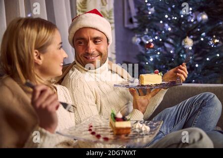 Handsome man in Santa hat resting with charming female in home Stock Photo