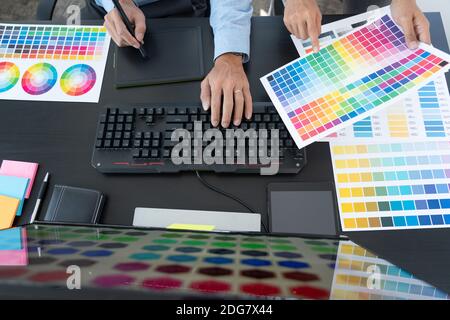 graphic designer team working on web design using color swatches editing artwork using tablet and a stylus at desks In creative office. Stock Photo