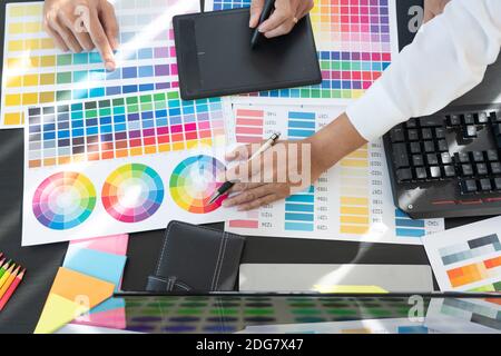 graphic designer team working on web design using color swatches editing artwork using tablet and a stylus at desks In creative office. Stock Photo