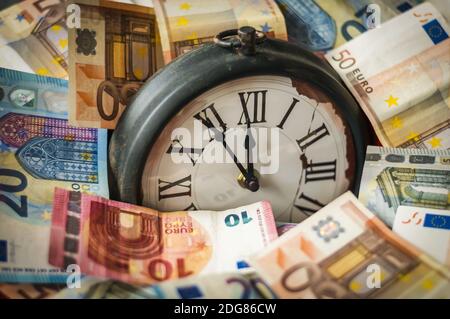 Euro currency and a clock, the hands stand five minutes before twelve. Stock Photo