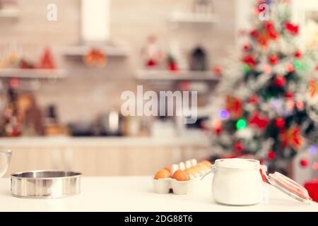 Ingredients for preparation of delicious cookies on table in empty room. Kitchen on christmas day with nobody in the room decorated with x-mas tree and garlands Stock Photo
