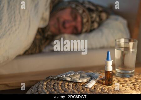A man lying with cold in bed lying in front of him medicines, selective focus. Stock Photo