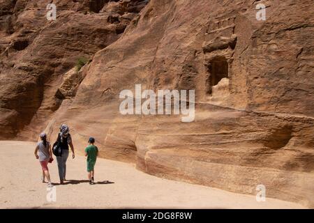 Family walks down the canyon of ancient city of Petra with  stone carvings  sandstone on sunny day in Jordan Stock Photo