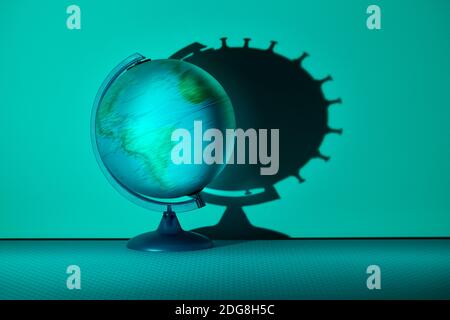 Spinning globe casting coronavirus biological cell shadow on wall Stock Photo