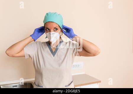 Healthcare worker girl is dressed in protective uniform, surgical cap, latex gloves and mask Stock Photo