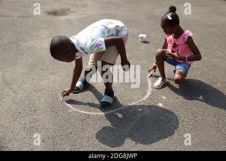 Brother and sister playing with sidewalk chalk on sunny pavement Stock Photo