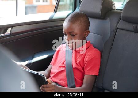 Boy using digital tablet in back seat of car Stock Photo