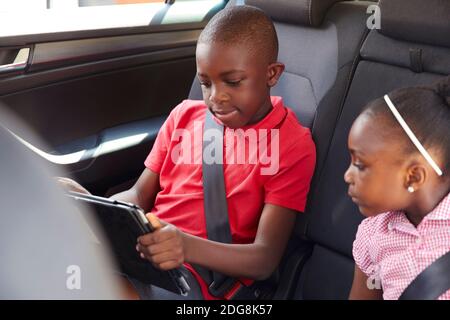 Brother and sister using digital tablet in back seat of car Stock Photo