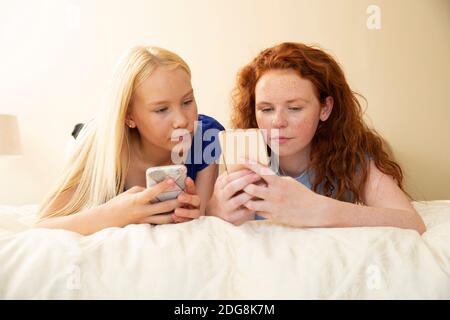Preteen girl friends using smart phones on bed Stock Photo