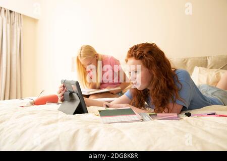 Preteen girl friends with digital tablet doing homework on bed Stock Photo