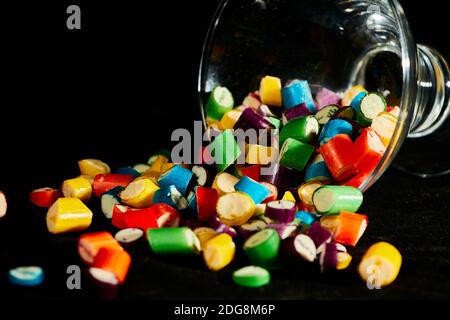 sugar candies falling from glass container on black table background. Empty space for text Stock Photo