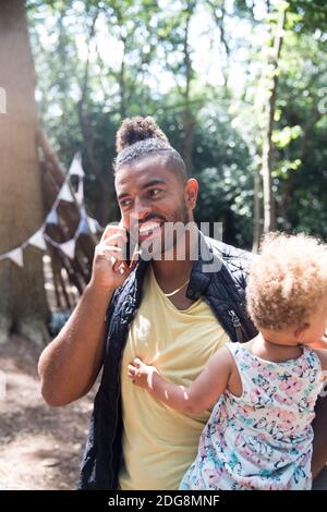 Smiling father holding toddler daughter and talking on smart phone Stock Photo