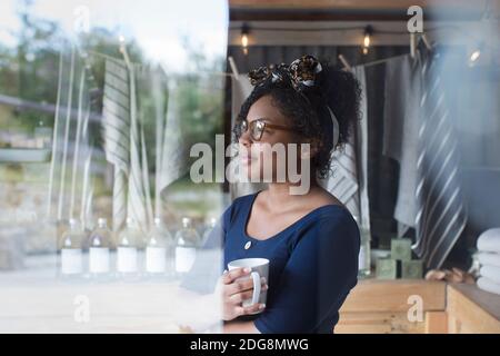 Thoughtful female shop owner drinking coffee at window Stock Photo
