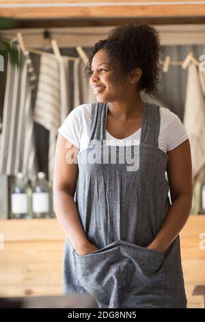 Portrait happy female shop owner in apron looking away Stock Photo