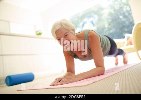 Portrait happy senior woman practicing plank pose on yoga mat at home Stock Photo