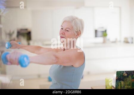 Senior woman exercising with dumbbells in kitchen Stock Photo