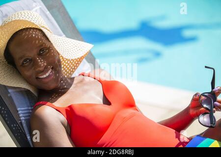 Portrait happy mature woman in sun hat sunbathing at sunny poolside Stock Photo