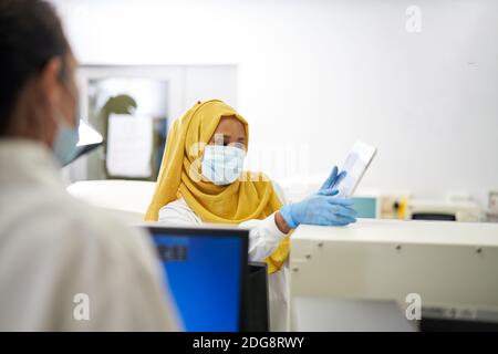 Female scientist in hijab and face mask using digital tablet Stock Photo