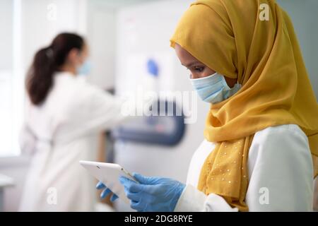 Female scientist in hijab and face mask using digital tablet Stock Photo