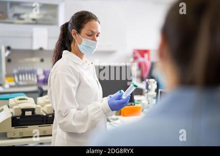 Female scientist in face mask examining specimen in laboratory Stock Photo
