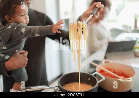 Father holding cute baby girl reaching for pasta noodles Stock Photo