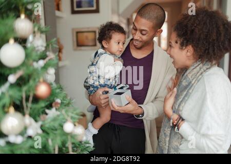 Happy parents and baby daughter opening Christmas gifts by tree Stock Photo