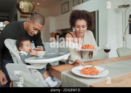 Couple eating spaghetti and feeding baby daughter at dining table Stock Photo