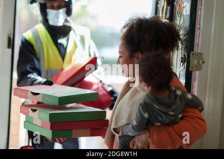 Mother with baby daughter receiving pizza from delivery man in mask Stock Photo