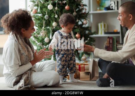 Happy parents and baby daughter opening Christmas gift by tree Stock Photo
