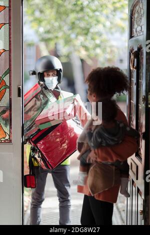 Mother with baby daughter receiving pizza from delivery person in mask Stock Photo