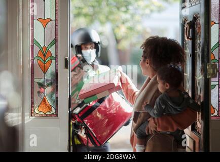 Woman with baby daughter receiving pizza from delivery man in mask Stock Photo
