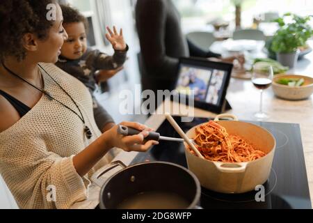 Mother and baby daughter cooking spaghetti and video chatting Stock Photo
