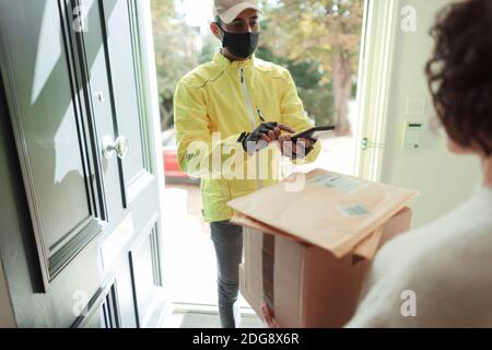 Woman receiving packages from delivery man in face mask at front door Stock Photo