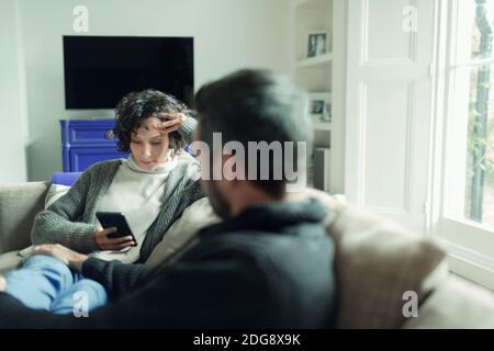 Couple relaxing and using smart phone on living room sofa Stock Photo