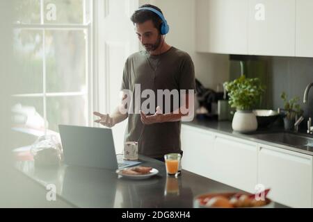 Man with headphones working from home video conferencing at laptop Stock Photo