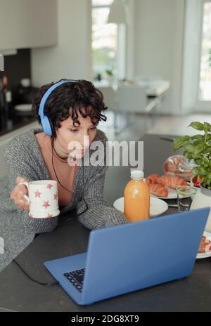 Woman with headphones working from home at laptop in morning kitchen Stock Photo