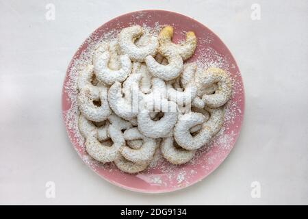 A pale pink plate of Vanillekipferl (small, crescent shaped Christmas sweets made with ground nuts and vanilla) on white background. Stock Photo