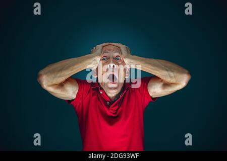 Head in hands. Portrait of crazy scared and shocked caucasian man isolated on dark background. Copyspace for ad. Bright facial expression, human emotions concept. Watching horror on TV, cinema. Stock Photo