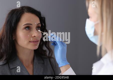 Beautician applies white cream to patient's face with cotton swab Stock Photo