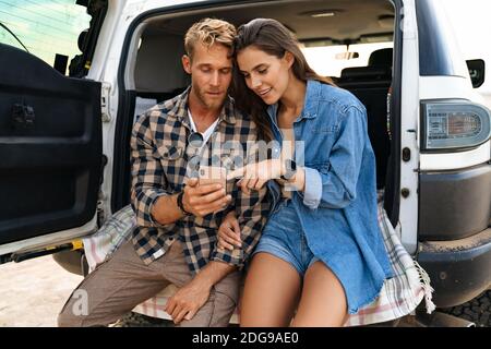 Beautiful couple sitting at the back of car and using smart phones Stock Photo