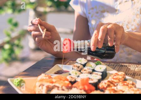 Woman with bottle of soy sauce sushi on the white plate in street cafe Stock Photo