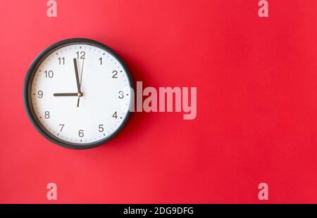 Round wall clock on red surface showing 9 o’clock, layout, top view, place for text Stock Photo