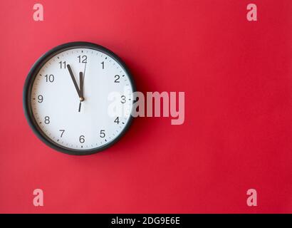 Round wall clock on red surface showing 12 o’clock, layout, top view, place for text Stock Photo