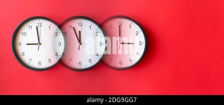 Round wall clocks on red surface showing 9, 12, 3, layout, top view, place for text Stock Photo