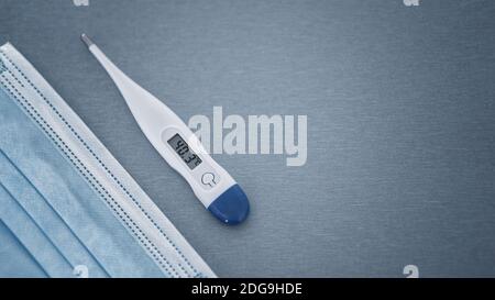 Flat lay of temperature display on digital thermometer with removal surgical face mask. Pandemic stay safe virus protection equipment concept copy spa Stock Photo