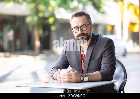 Happy middle age businessman portrait drinking a coffee outdoors in Bangkok, Thailand. Stock Photo