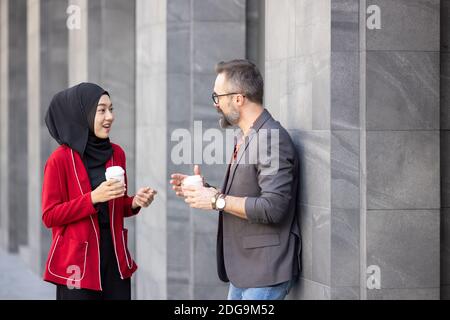 Handsome beard middle age caucasian businessman drinking coffee at outdoor coffee cafe with young beautiful hijab muslim women Stock Photo